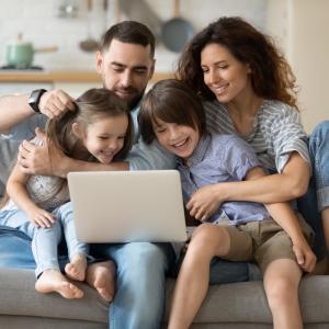 A family seated on a sofa in their living room with a laptop searching for home insurance policies.
