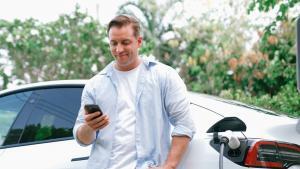 Electric car charging with a driver checking his phone, used for an article on electric vehicle insurance in Ireland.