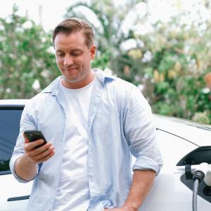 Electric car charging with a driver checking his phone, used for an article on electric vehicle insurance in Ireland.